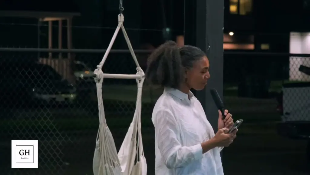 A host in white speaking into a microphone beside the hammock chairs in the yard at night