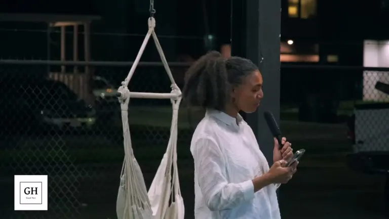 A host in white speaking into a microphone beside the hammock chairs in the yard at night