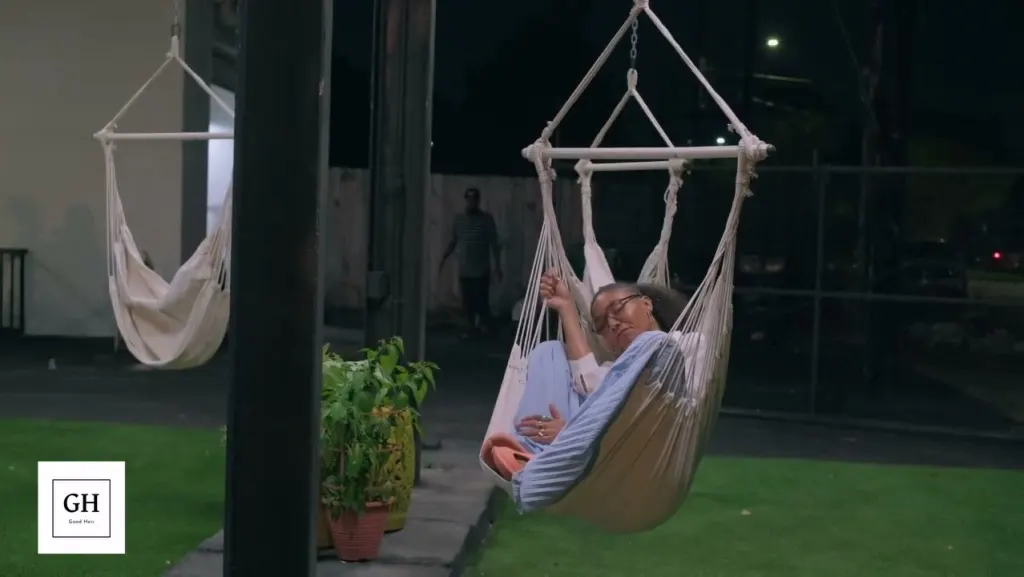 A guest relaxing in a white hammock chair on the turf yard at night, with potted plants beside the pavilion post