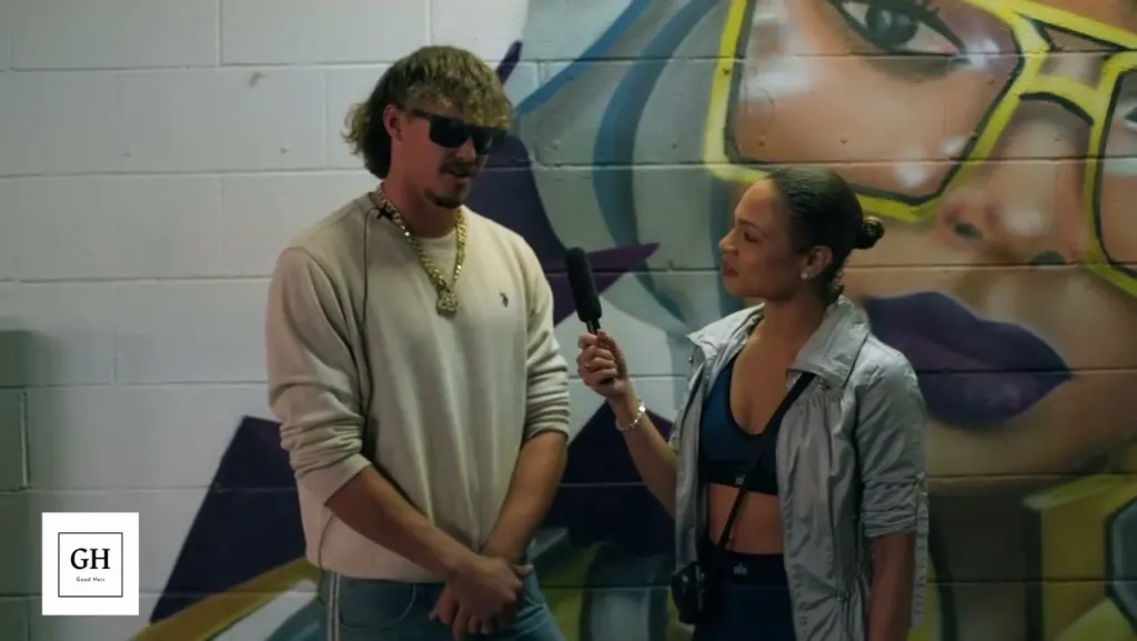 A guest being interviewed with a microphone in front of a large painted mural of a woman in yellow sunglasses