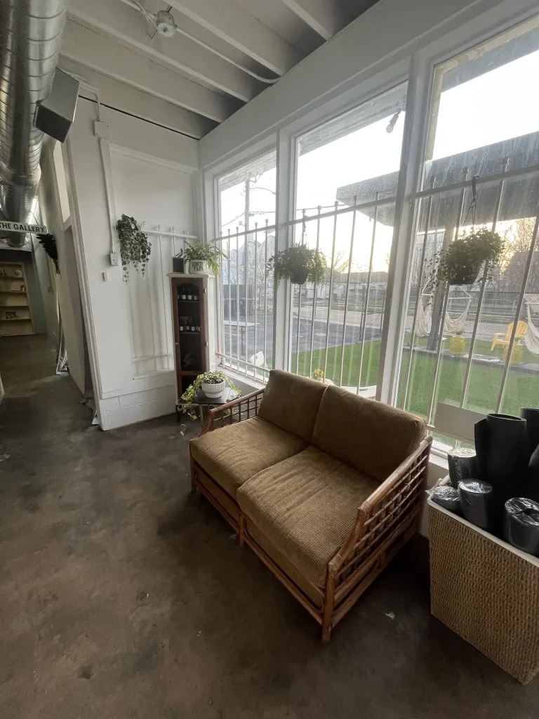 Sunroom lounge with floor-to-ceiling windows, a rattan loveseat with tan cushions and hanging plants, looking out to the turf yard